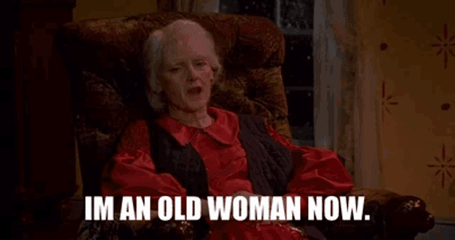an elderly woman is sitting in a chair with the words `` im an old woman now '' .