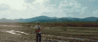 a man playing a guitar in a muddy field