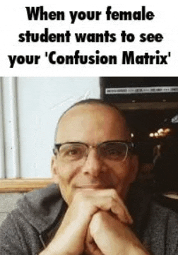 a man wearing glasses is sitting at a table with his hands folded in front of his face .