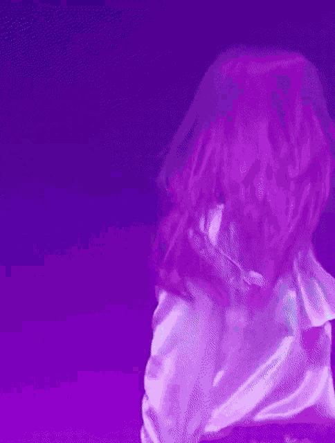 a woman in a white satin shirt is dancing in front of a blue background .