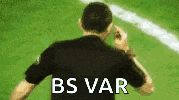 a man in a black shirt is standing on a soccer field with the words `` bs var '' written on his back .