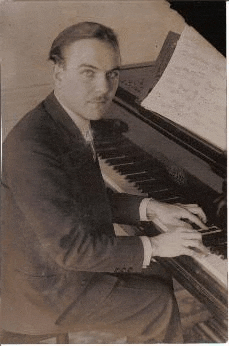 a man in a suit is sitting at a piano with sheet music on it .
