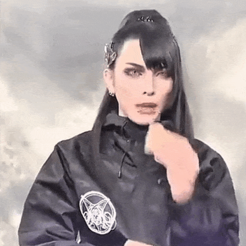 a woman is wearing a black jacket with a pentagram on it and making a funny face .