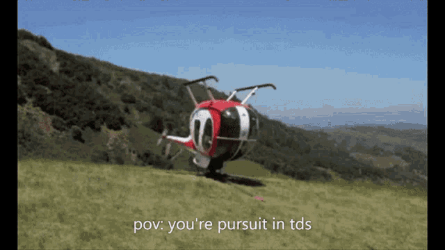 a red and white helicopter is flying over a grassy hillside with the words pov you 're pursuit in tds