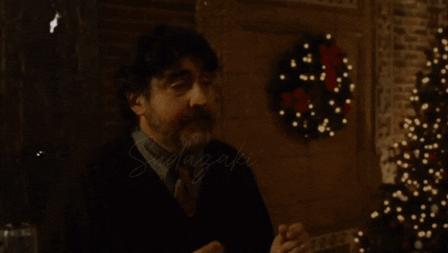 a man with a beard stands in front of a christmas tree and a wreath with the word sadazaki written on it