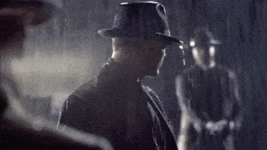a man wearing a fedora stands in the rain