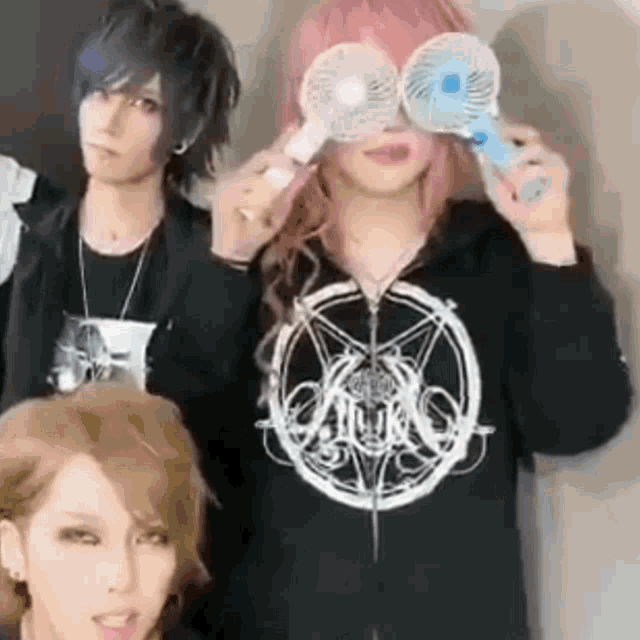 a group of people are standing next to each other and one of them is holding a fan in front of his eyes .
