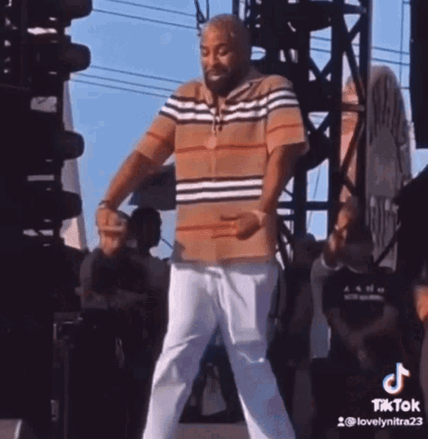 a man in a striped shirt and white pants is dancing on a stage at a concert .