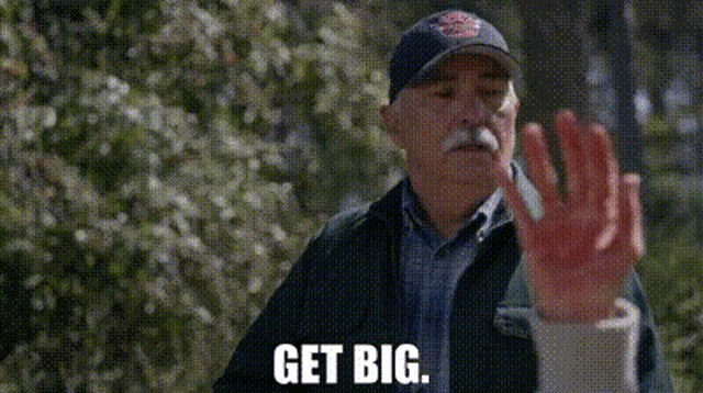 a man with a mustache is wearing a hat and a jacket and says get big .