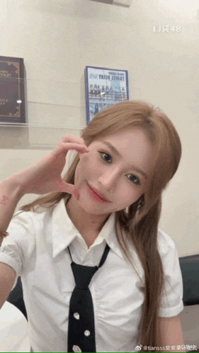 a woman wearing a white shirt and black tie making a heart shape with her hand