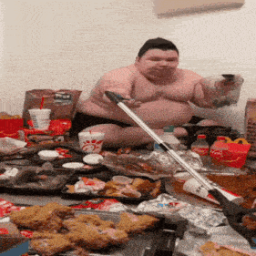 a very fat man is sitting on the floor surrounded by food and drinks including a bottle of coca cola