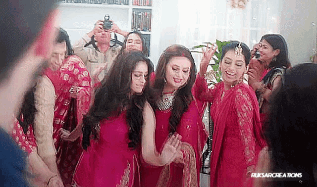 a group of women in red dresses are dancing in a room while a man takes a picture of them .