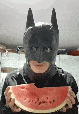 a man in a batman mask holding a slice of watermelon