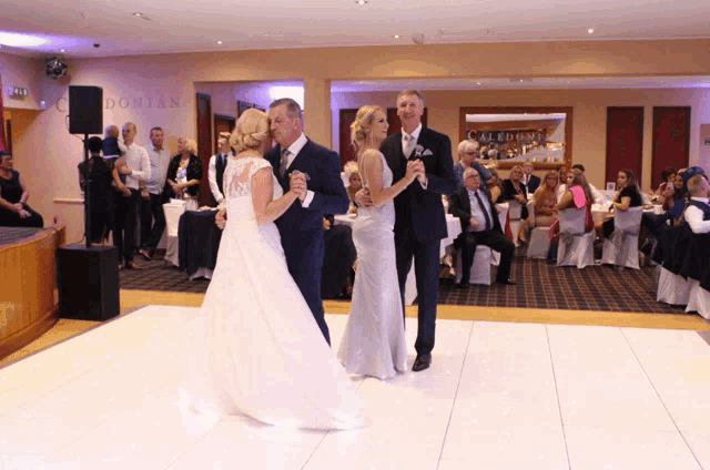 a bride and groom are dancing on a white dance floor in front of a wall that says caledonia