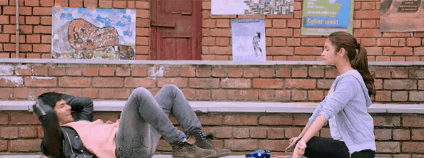 a woman sits next to a man laying on the ground