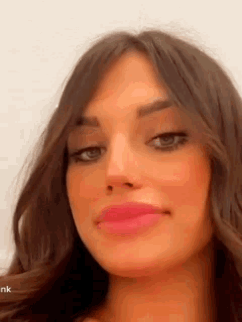 a close up of a woman 's face with long brown hair and pink lipstick .