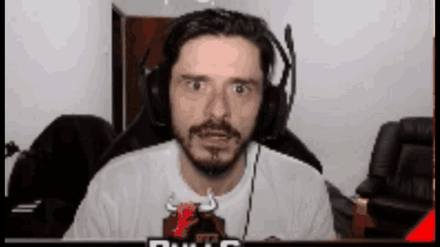a man with a beard is wearing headphones while sitting in front of a computer screen .