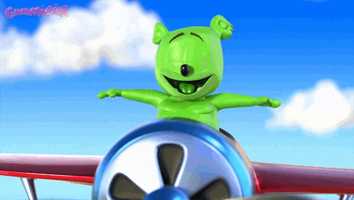 a green gummy bear is sitting on a plane with its arms outstretched and the word gummy bear on the bottom right