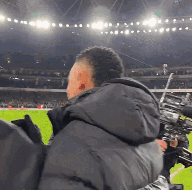 a man in a black jacket is watching a soccer game in a stadium