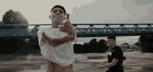 a man with a tattoo on his stomach is standing in front of a blue bridge