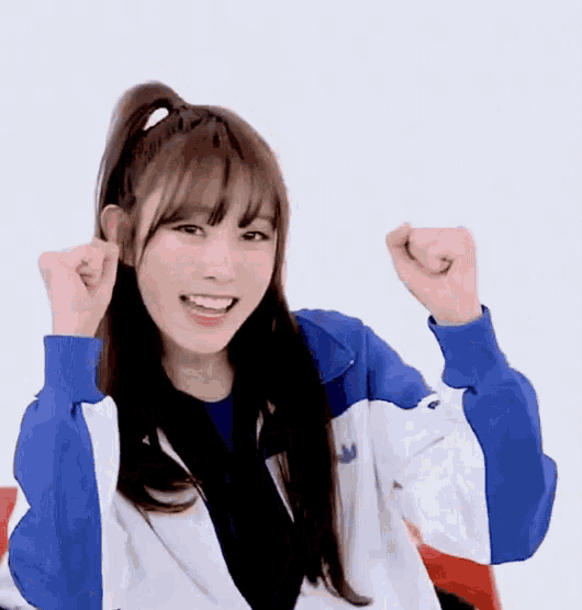 a girl in a blue and white jacket is smiling and holding her fist in the air .