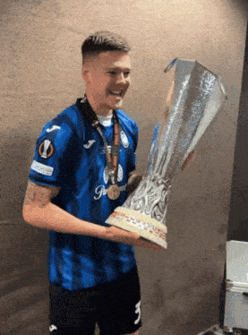 a man in a blue jersey with the number 3 on it holds a large trophy