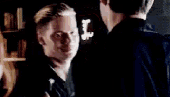 two men are standing next to each other in a dark room and talking to each other .