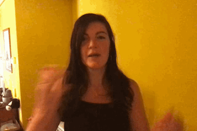 a woman stands in front of a yellow wall with her hands outstretched
