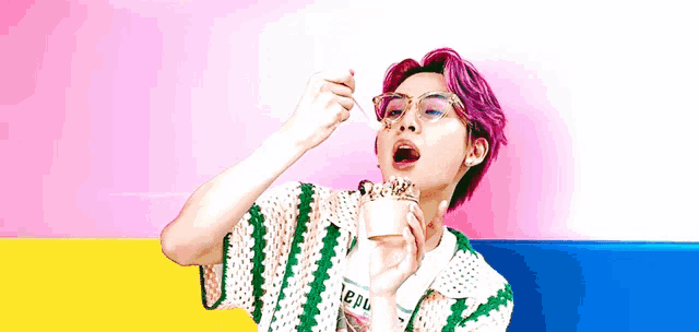 a man with pink hair and glasses is eating ice cream with a spoon