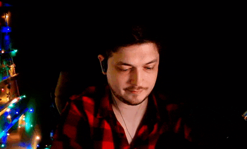 a man in a red plaid shirt is sitting in front of a christmas tree and wearing headphones .