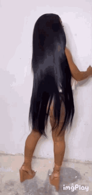 a woman with very long black hair is standing in front of a white wall wearing wedges .