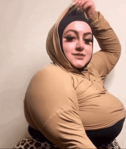 a woman wearing a hijab and a hoodie is standing in front of a wall