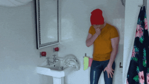 a man in a yellow shirt and red hat is standing in a bathroom next to a sink