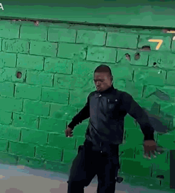 a man is standing in front of a green brick wall .