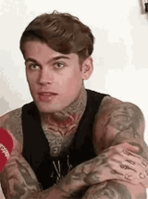 a man with a lot of tattoos on his arms is sitting down with his arms crossed .