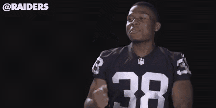 a man in a raiders jersey is dancing with his arms outstretched in the dark .