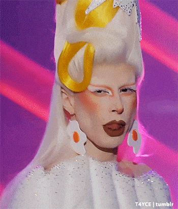 a drag queen wearing a white dress and earrings with eggs on them .