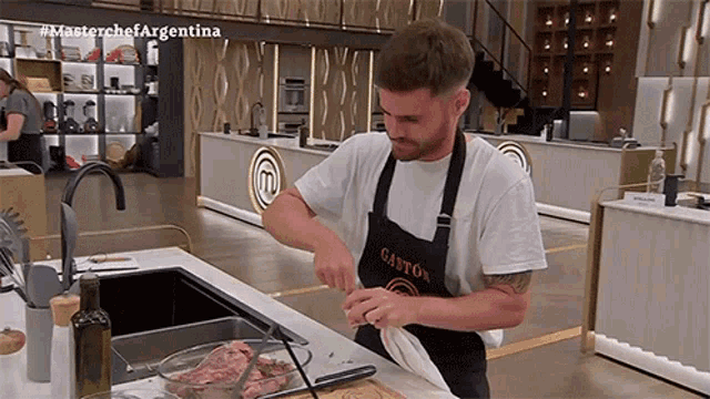 a man wearing an apron that says gaston is cutting a piece of meat