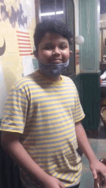 a young boy wearing a yellow and blue striped shirt and a mask on his face