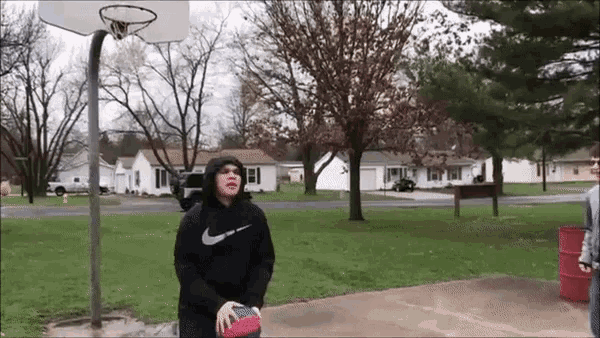 a man in a nike hoodie is playing basketball in a park