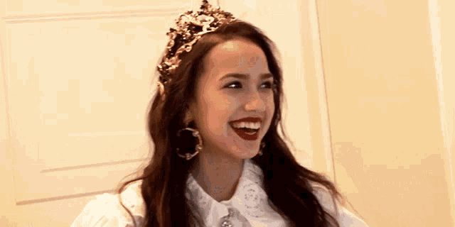a woman wearing a tiara and hoop earrings is smiling .