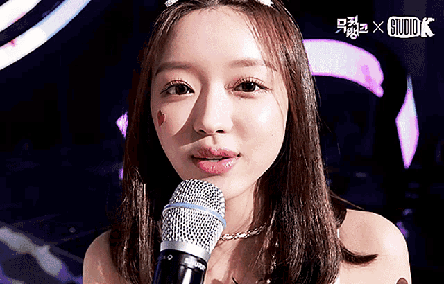 a close up of a woman holding a microphone with a studio k logo behind her