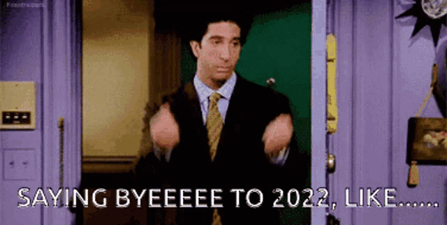 a man in a suit and tie is standing in a doorway and saying byeeee to 2022 , like .