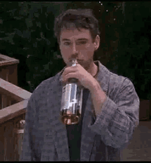 a man in a robe is drinking a bottle of whiskey .