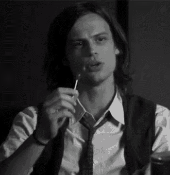 a man in a white shirt and tie is holding a lollipop in his mouth .