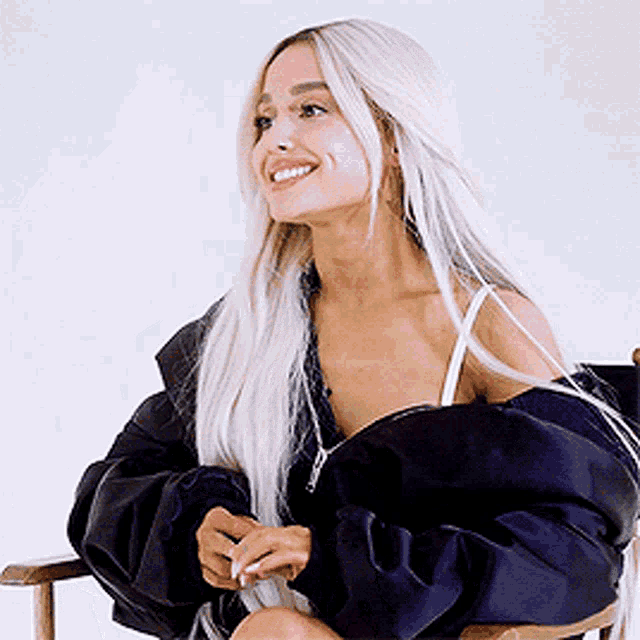 ariana grande is sitting in a chair with her legs crossed and smiling .