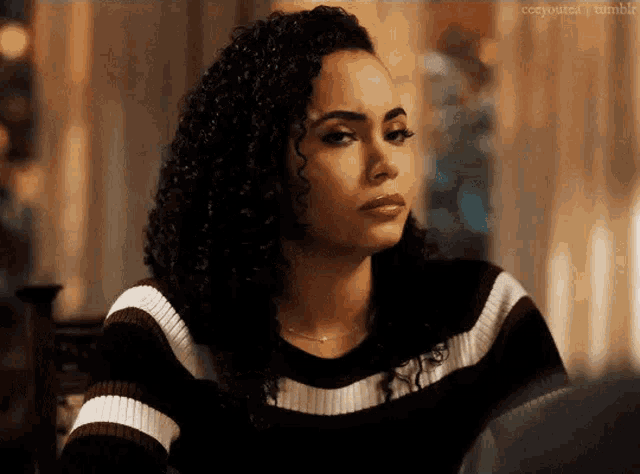 a woman with curly hair and a striped sweater is sitting at a table .