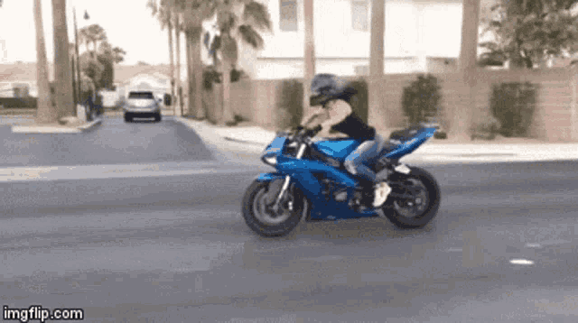 a woman is riding a blue motorcycle down a street with a car behind her