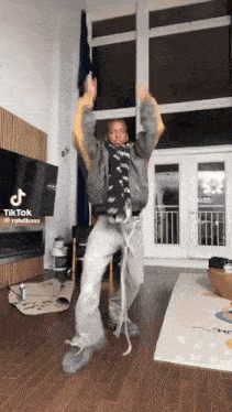 a man is dancing in a living room with a tiktok watermark at the bottom