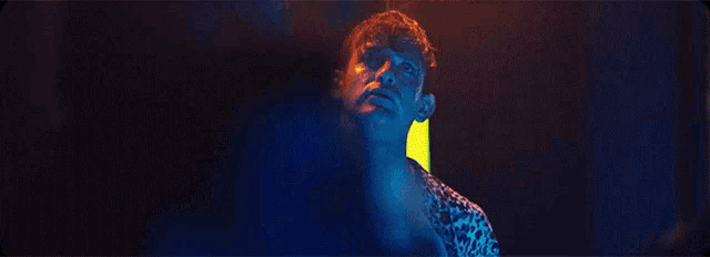 a man in a leopard print shirt is standing in a dark room with blue lights behind him .